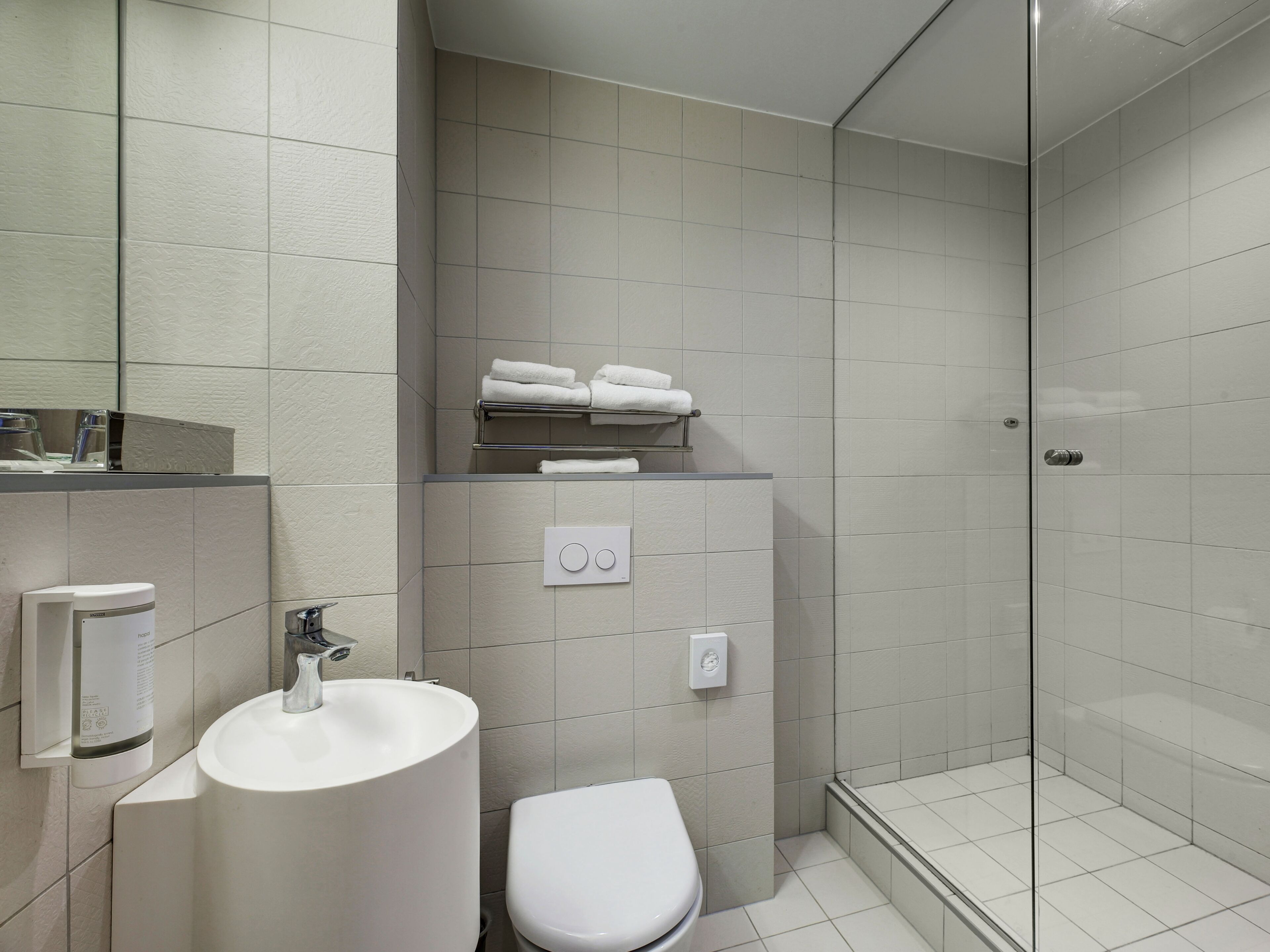 Et moderne badeværelse med hvid vask, toilet og glasbrusekabine.