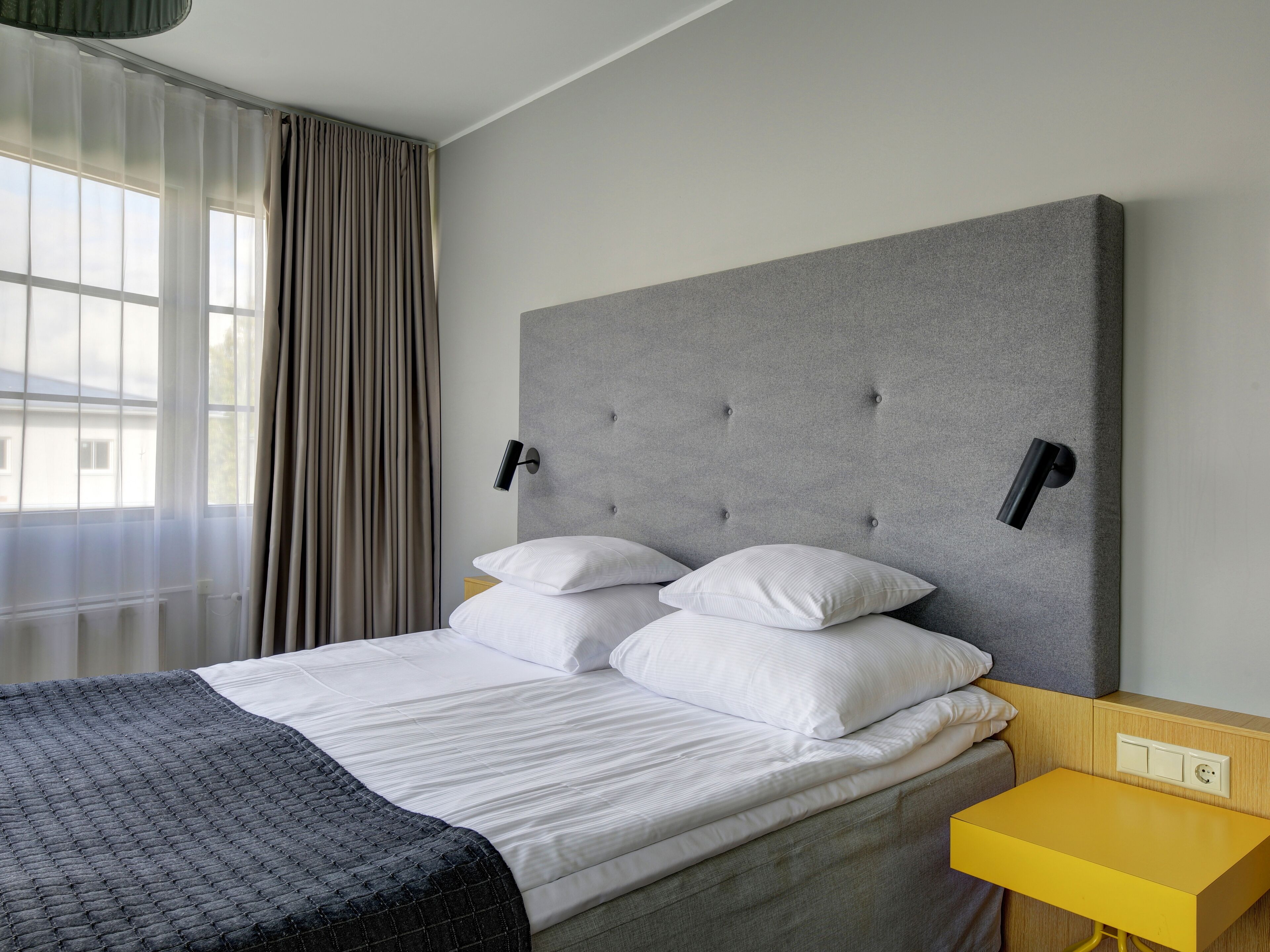 A modern hotel room with a large bed, two bedside tables, and a small desk.