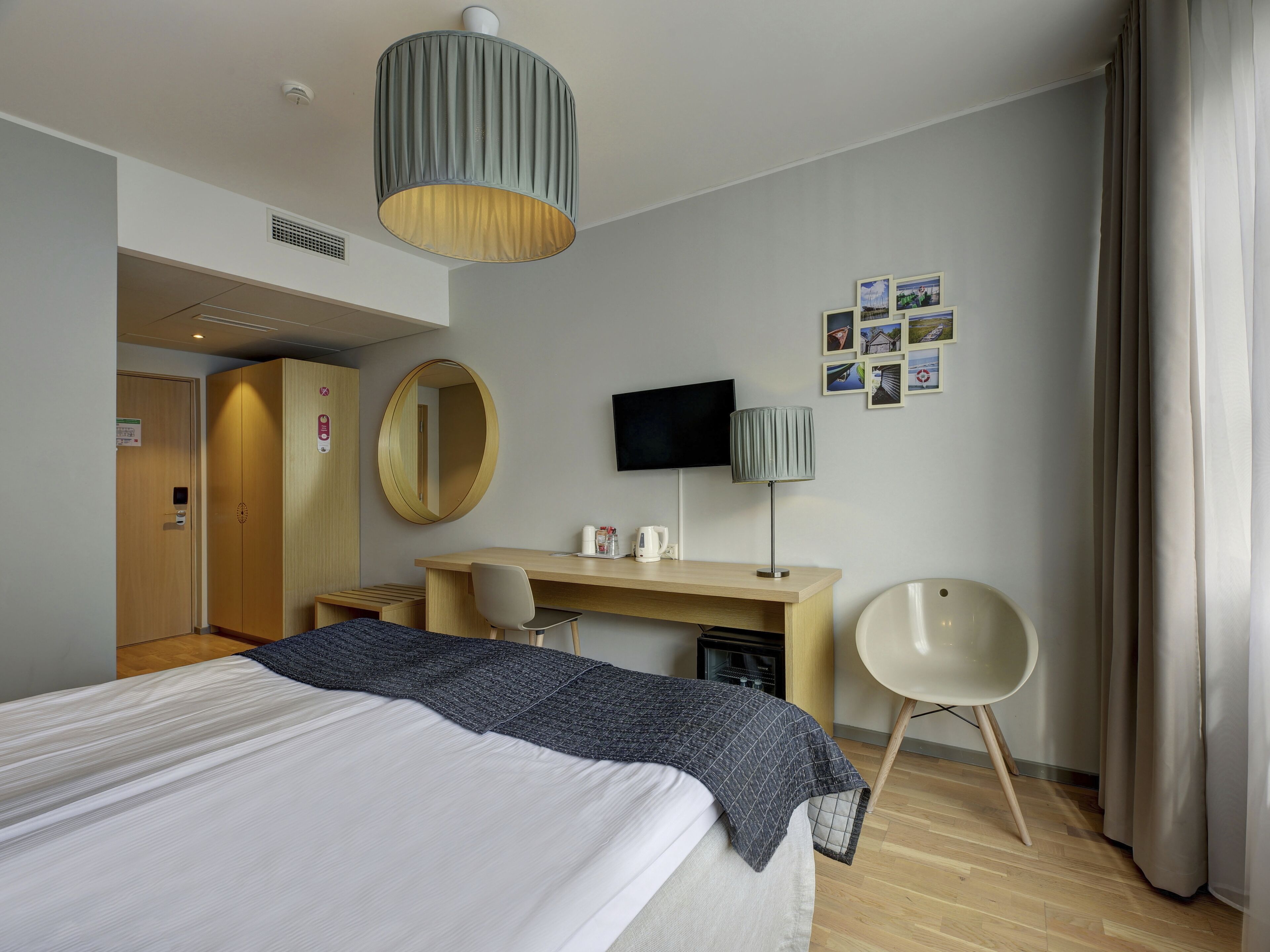 A modern hotel room with a bed, desk, chair, and a television on the wall.