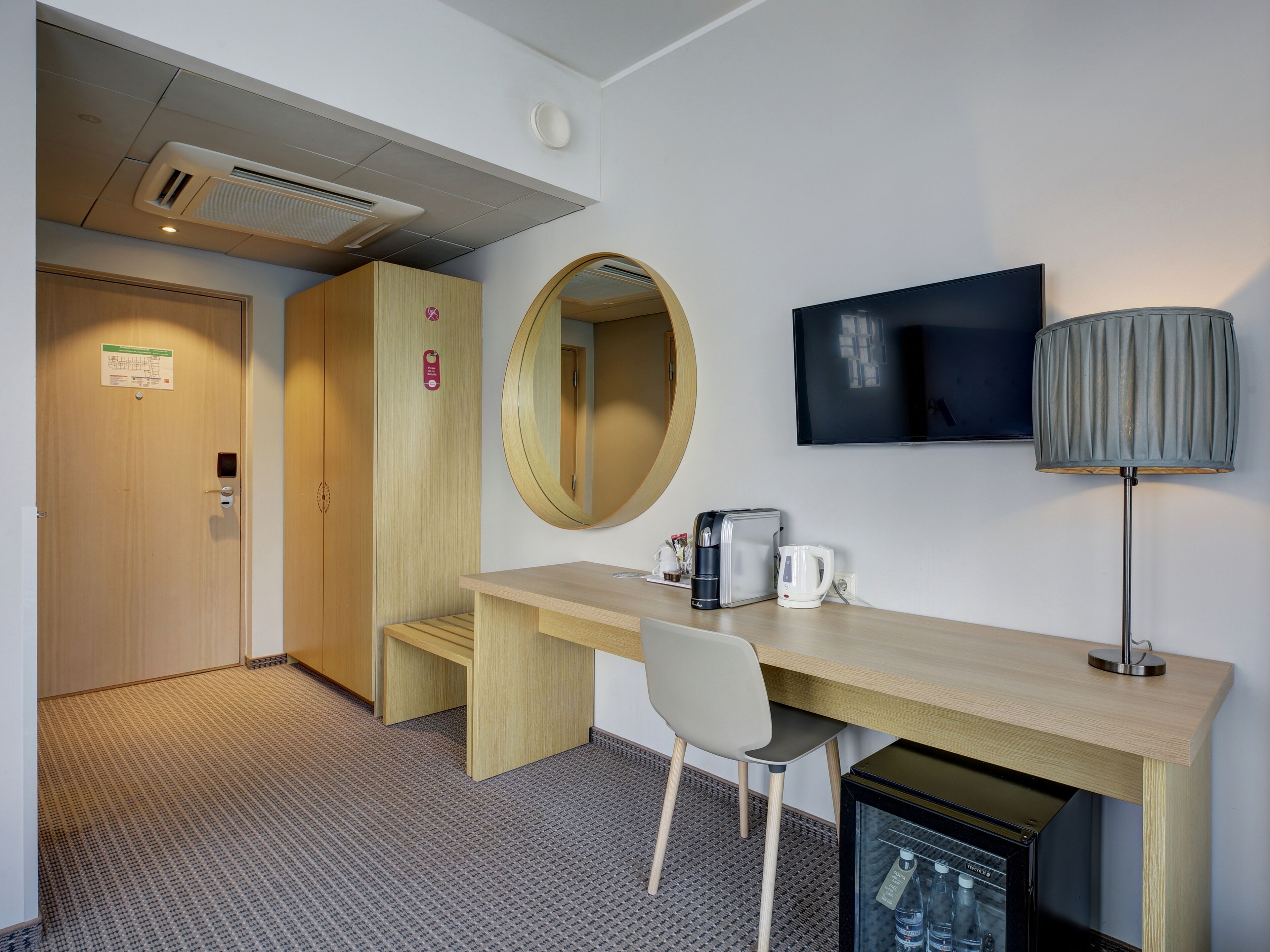 Hotelkamer met een houten bureau, een stoel, een flatscreen televisie, een lamp, een koffiezetapparaat en een minibar.