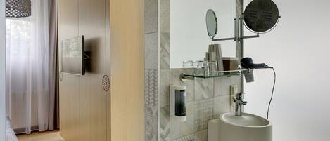 A modern bathroom with a glass shelf holding toiletries, a round mirror, and a sink.