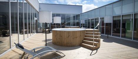 A wooden deck with a hot tub, lounge chairs, and a staircase leading to an upper level.