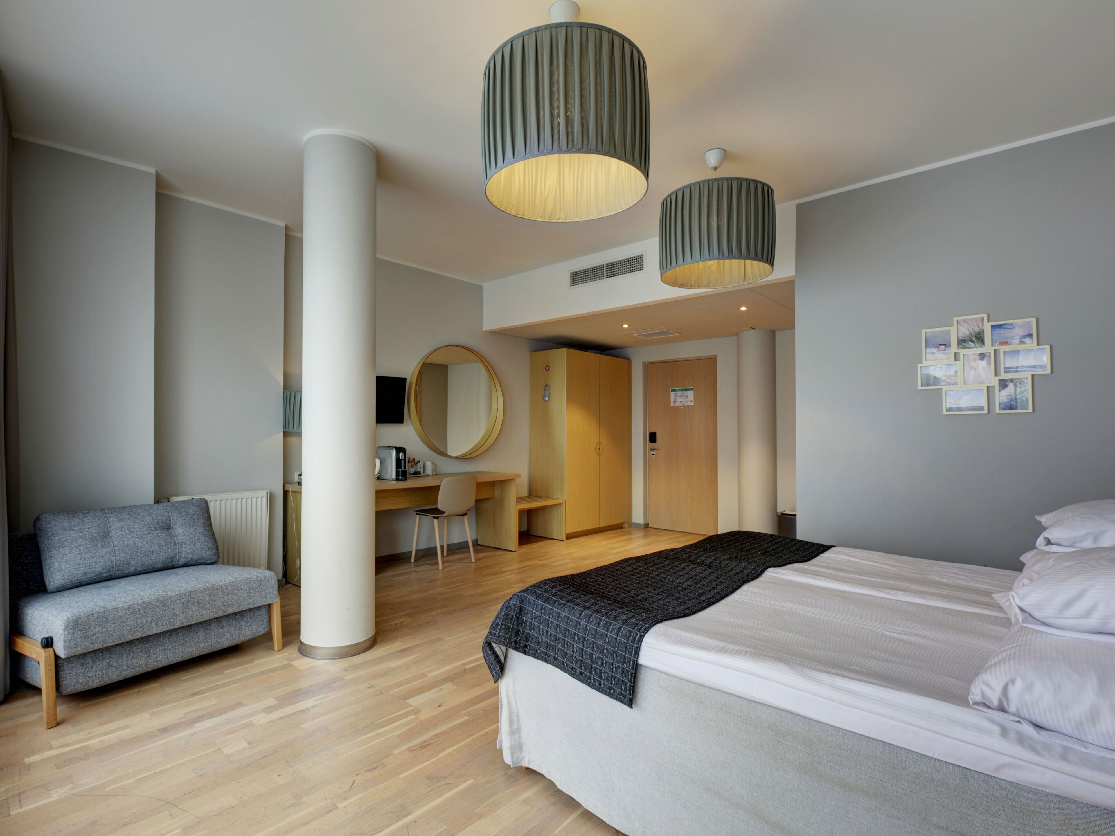 A modern hotel room with a bed, a desk, a chair, and a large mirror.
