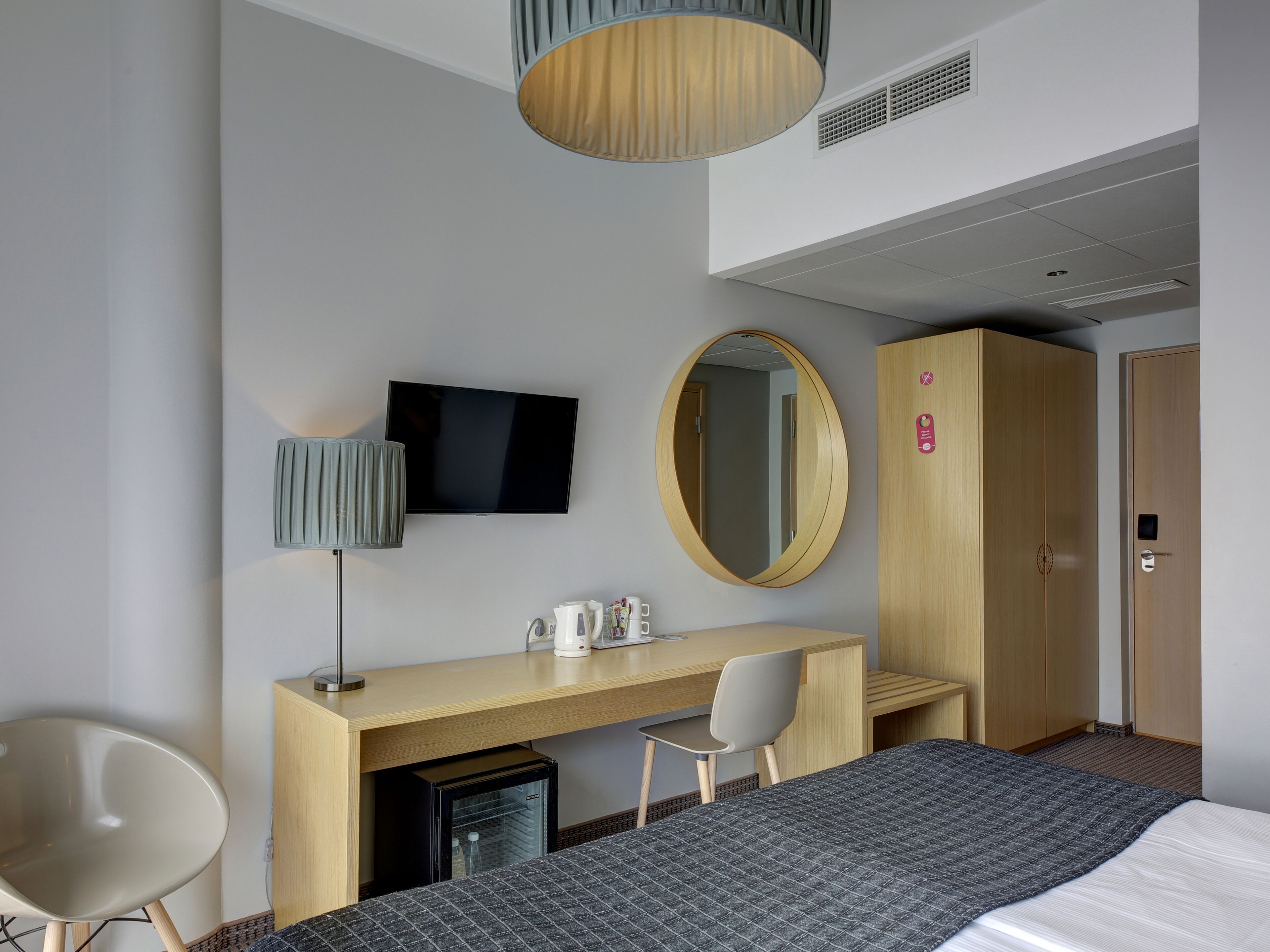 Una habitación de hotel con cama, escritorio con computadora, televisor, espejo y armario.