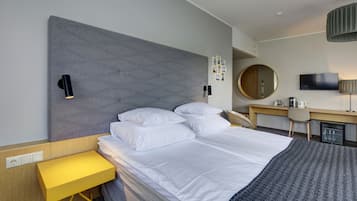 A modern hotel room with a large bed, a desk, a chair, a television, and a small refrigerator.