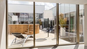 A modern outdoor area with a wooden staircase, lounge chairs, and a glass wall offering a view of a building. - Estonia Resort Hotel & Spa (Parnu)