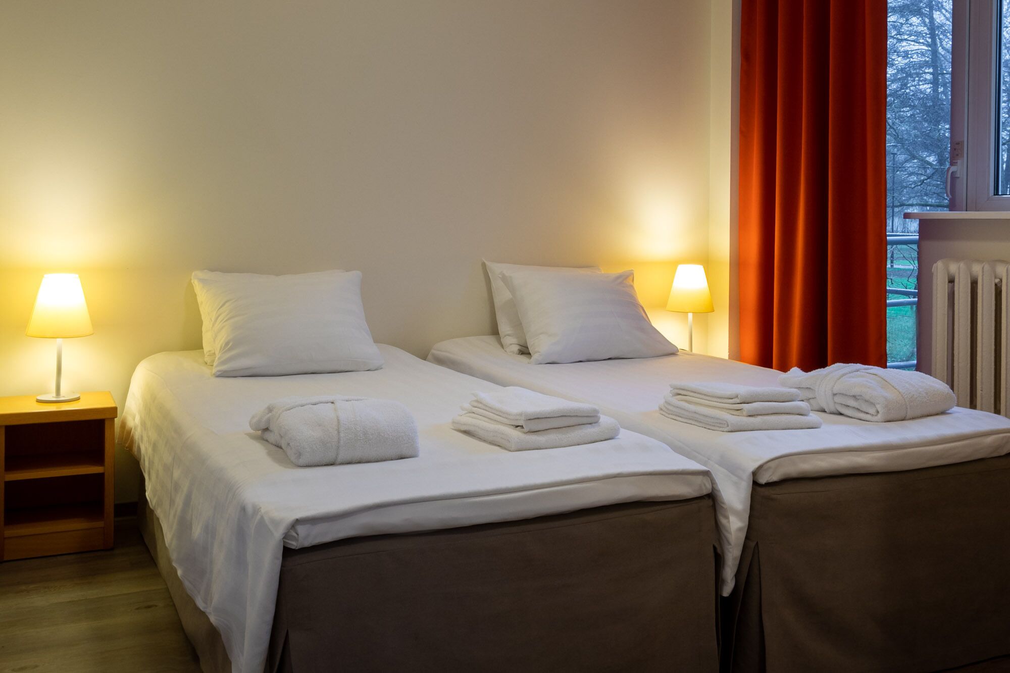 A hotel room with two beds, each with white linens and pillows, and two bedside lamps.