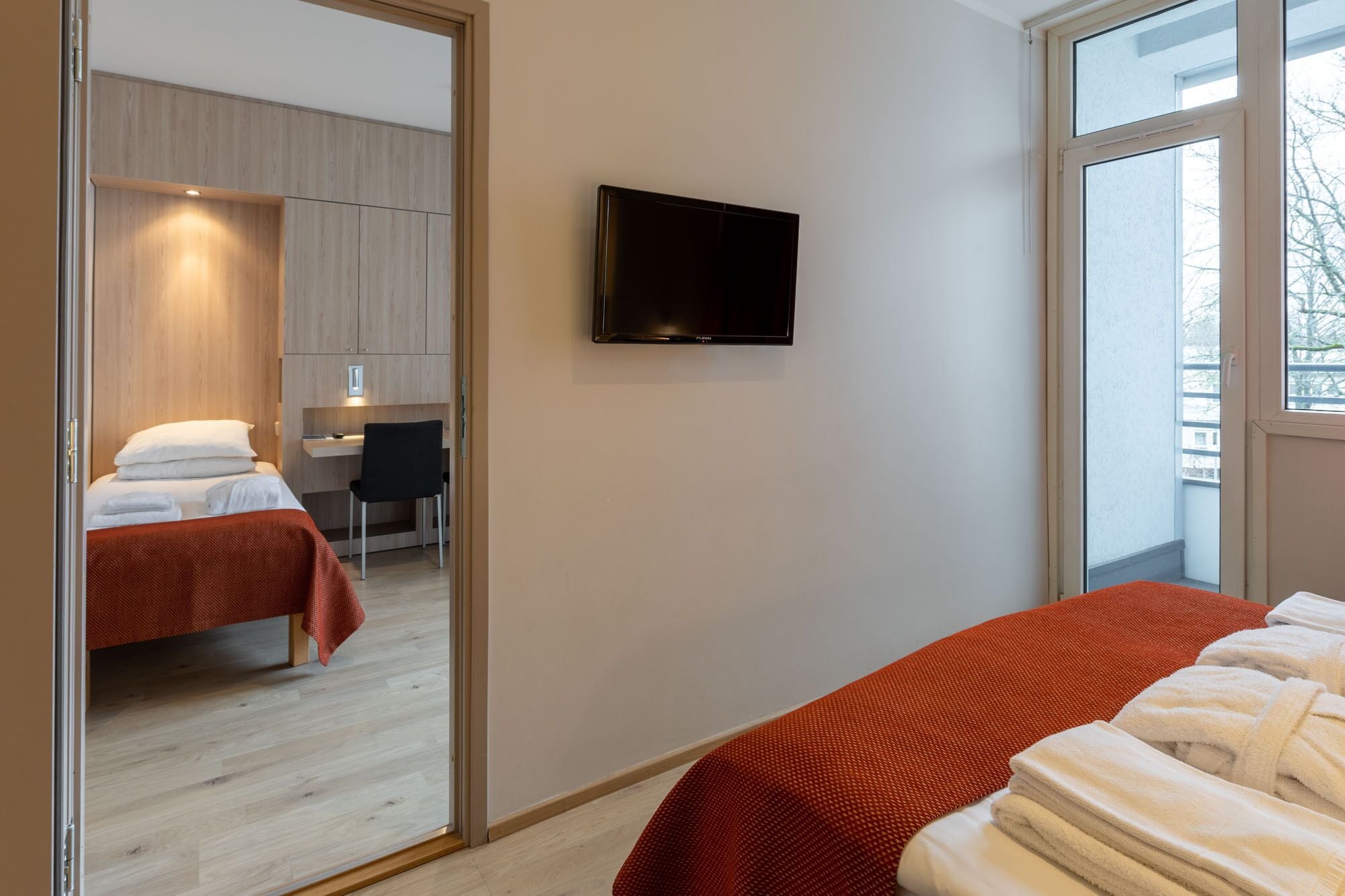 A modern hotel room with a large bed, a desk, a chair, and a TV on the wall.