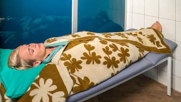 Una persona acostada en una cama en una habitación con pared azul y suelo de baldosas.
