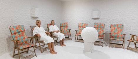 A room with six wooden chairs with floral upholstery, arranged in a semi-circle around a central white sculptural object.