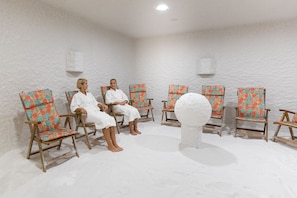 Een kamer met zes houten stoelen met bloemenstoffering, gerangschikt in een halve cirkel rondom een centraal wit sculptuur.