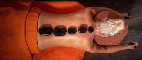 A person receiving a back treatment with multiple stones placed along their spine.