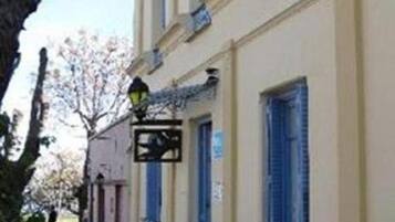 Un bâtiment à la façade jaune, aux volets bleus et à la grille en métal.
