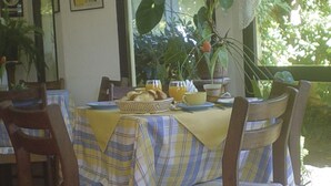 A dining area with a table set for two, featuring a striped tablecloth, wooden chairs, and a basket of bread. - Posada del Angel (Colonia del Sacramento)