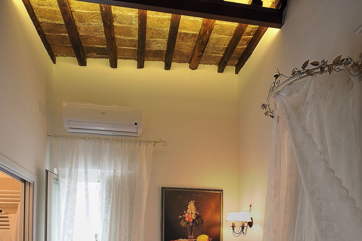 A bedroom with a floral bedspread, a painting on the wall, and a ceiling with exposed beams.