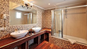 Une salle de bain moderne avec un mur en pierre derrière le plan de travail, un grand miroir, deux vasques et une douche à l’italienne.