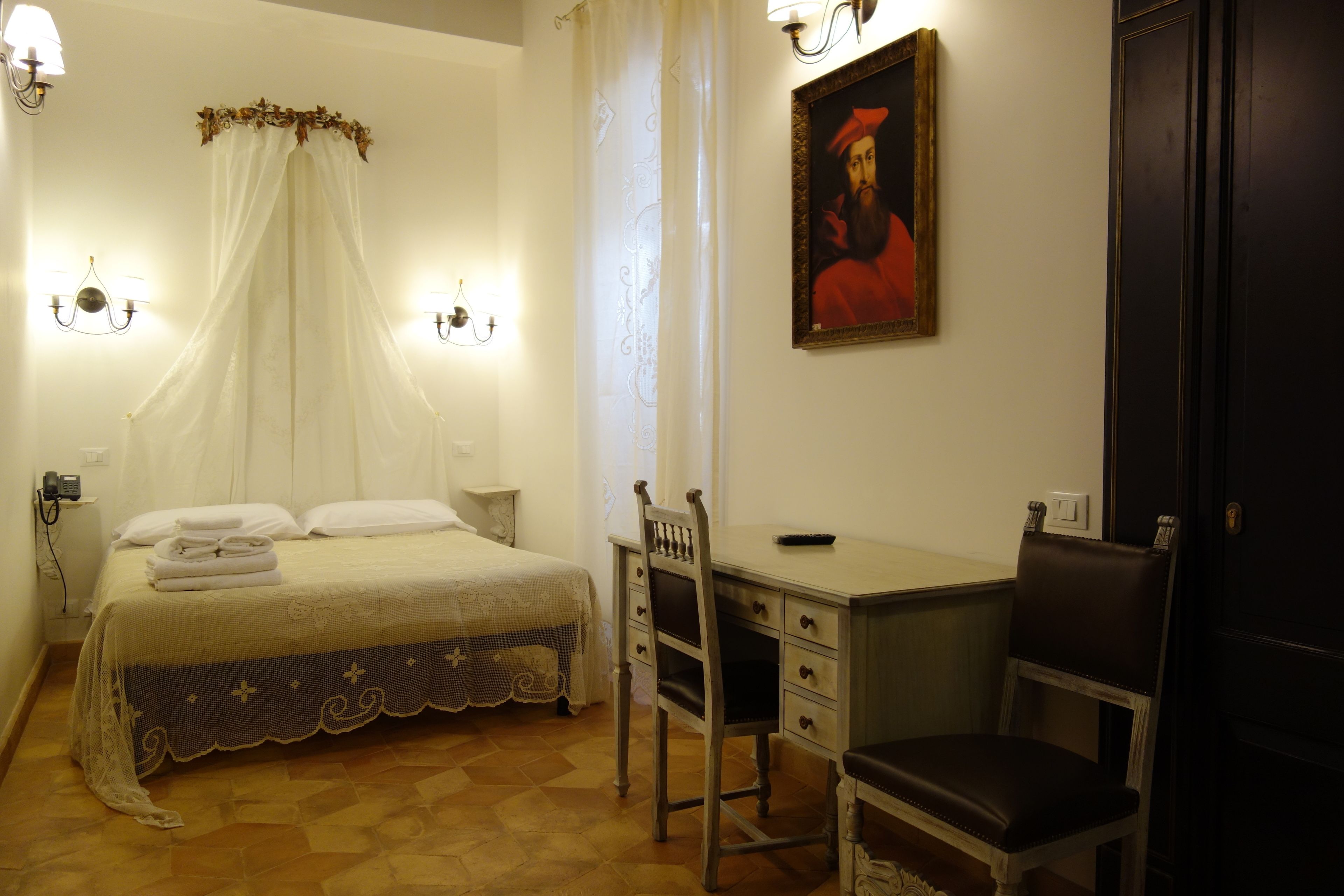 A bedroom with a bed, bedside table, chair, desk, and a painting on the wall.