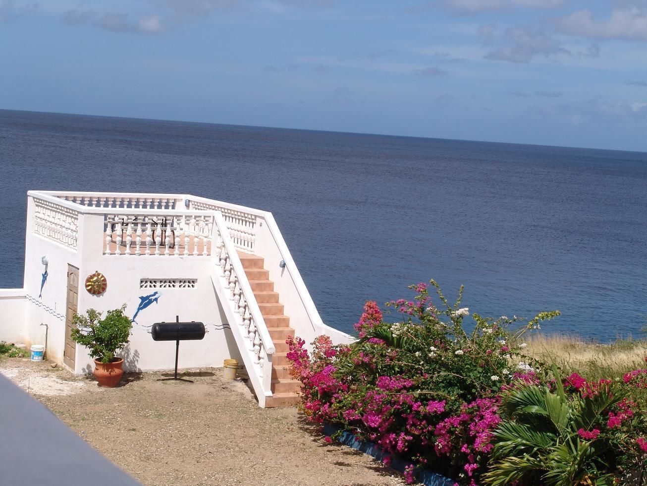 A white building with a staircase leading to a balcony overlooking the sea.