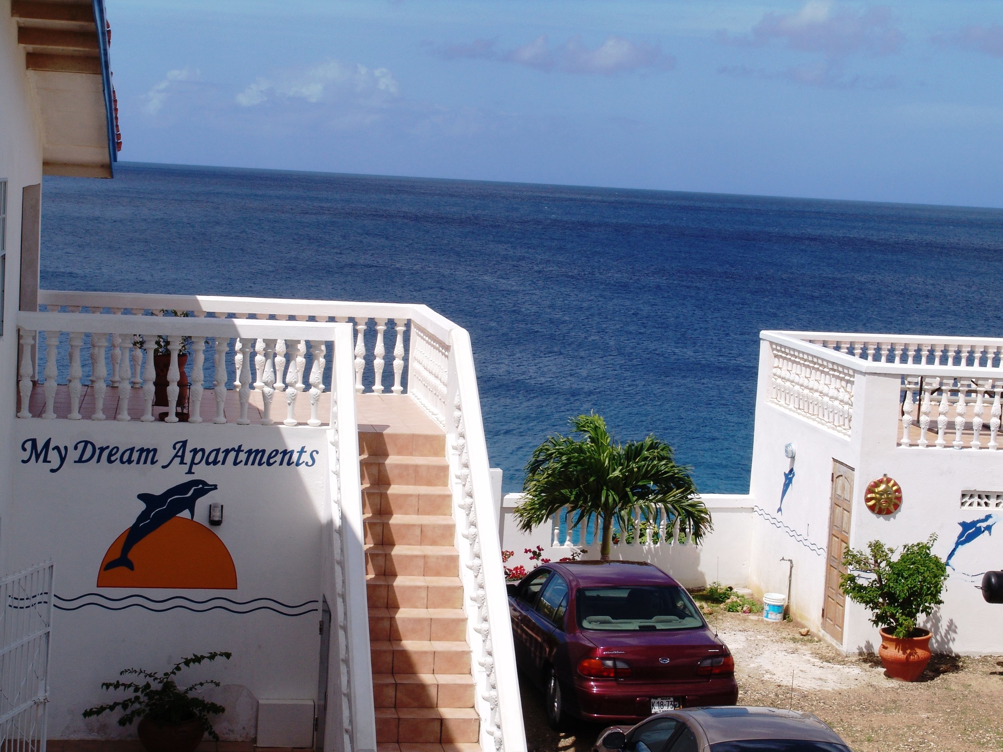 Un immeuble situé sur la côte, avec une enseigne indiquant « My Dream Apartments », un escalier, une voiture garée et une vue sur la mer.