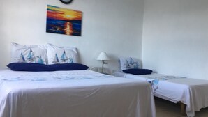 Hotellihuone, jossa on kaksi sänkyä. Jokaisessa sängyssä on sängynpeitteessä purjelaivamotiivi, ja huoneessa on yöpöytä, lamppu sekä seinällä oleva taulu, jossa on kuvattuna auringonlasku.