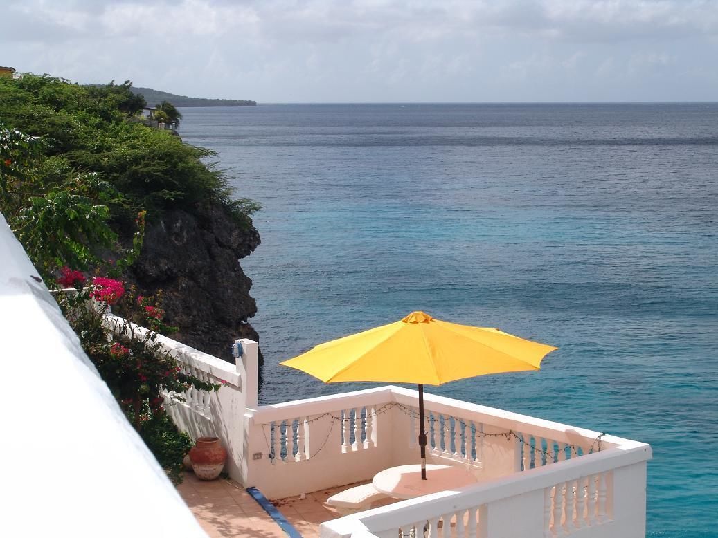 A balcony with a yellow umbrella overlooking a coastal view.