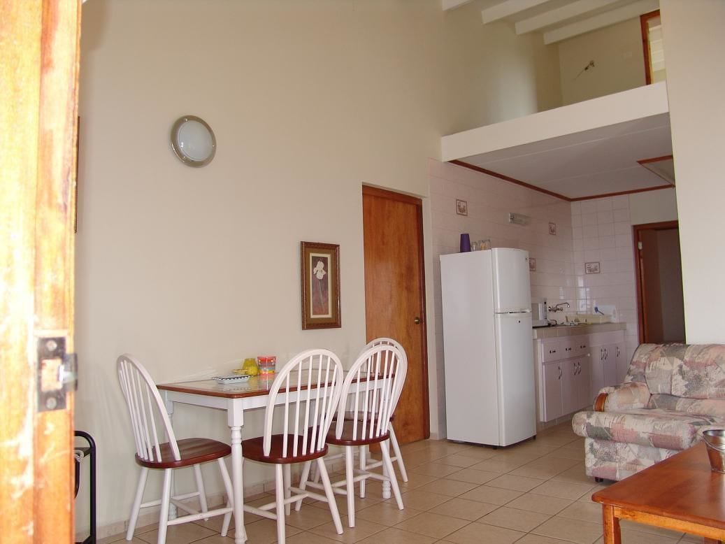 Un coin repas avec une table et des chaises, un réfrigérateur et, au fond, une cuisine.