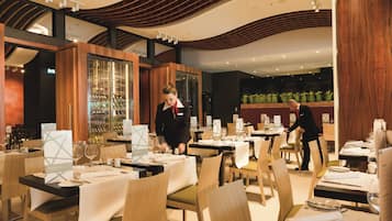 Un interior de restaurante moderno con paneles de madera, manteles blancos y mesas y sillas ordenadas.