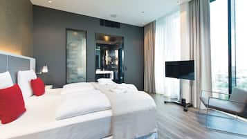 A modern hotel room with a large bed, a flat-screen TV, a seating area, and a city view.