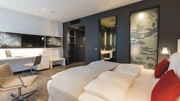 A modern hotel room with a large bed, a desk with a chair, and a walk-in closet.