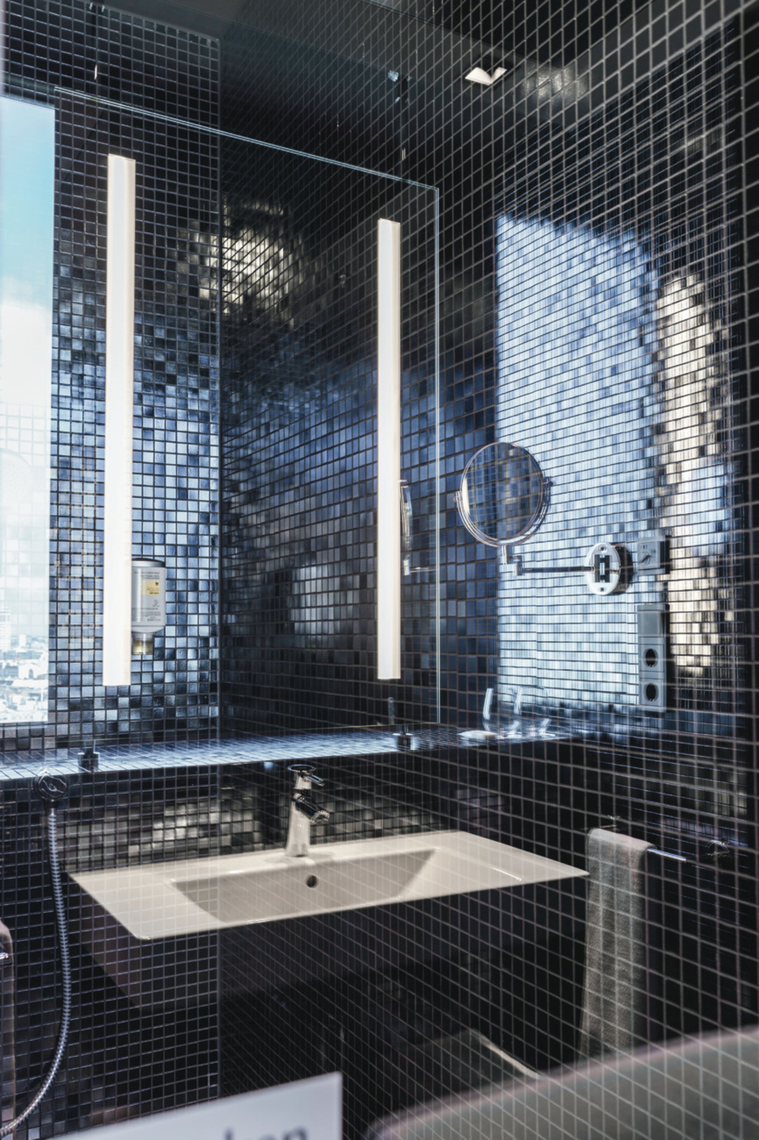 Un baño moderno con un salpicadero de azulejos negros, un espejo rectangular y un lavabo blanco.