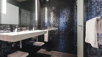 A modern bathroom with a large mirror, a white sink, and a tiled shower area.