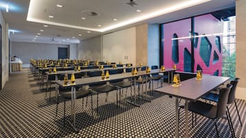 Une salle de conférence avec de longues tables, des chaises et des bouteilles d’eau jaunes.