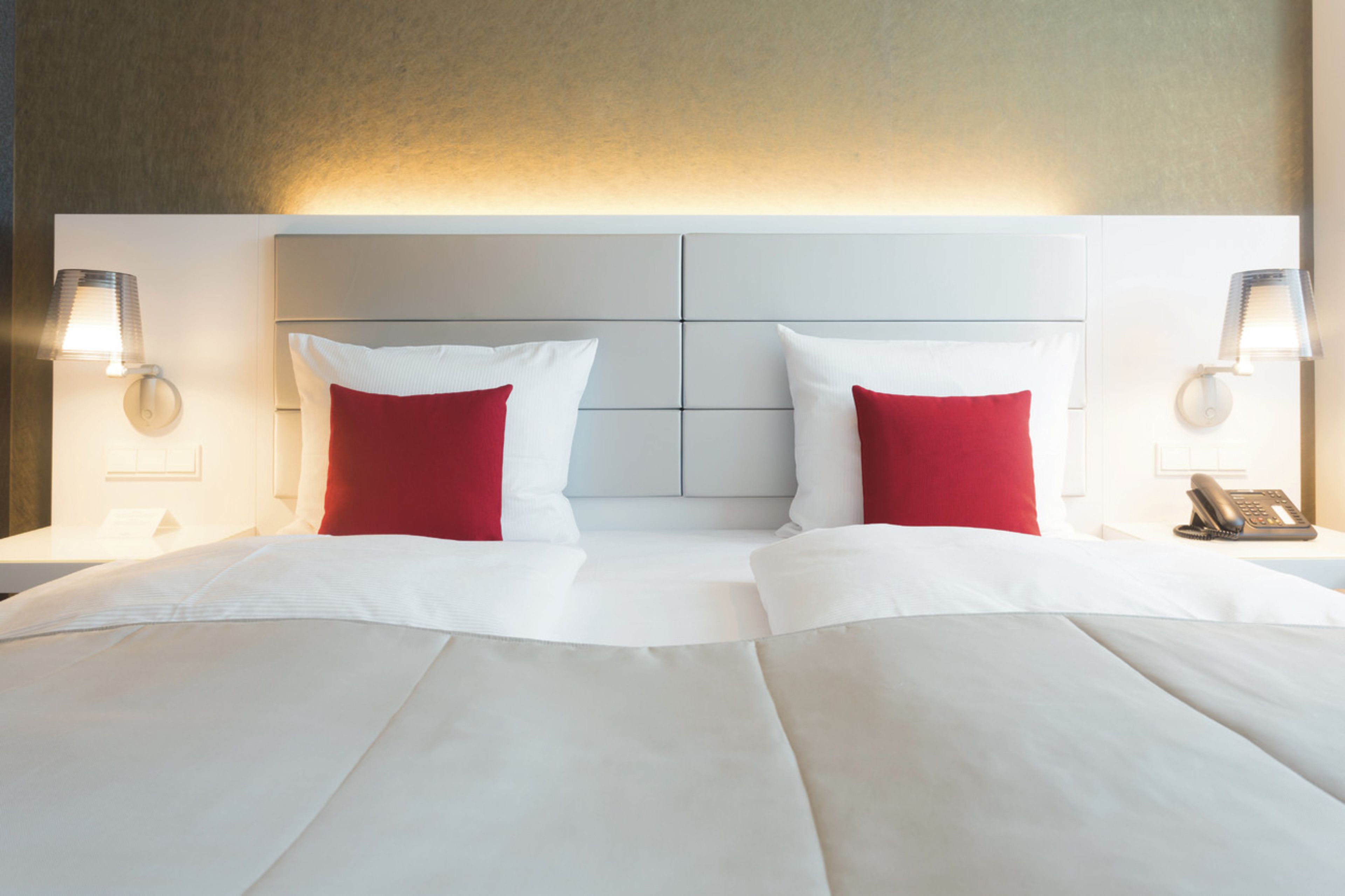 Ein Hotelzimmer mit einem großen Bett, zwei roten Kissen, weißer Bettwäsche und zwei Nachttischlampen.