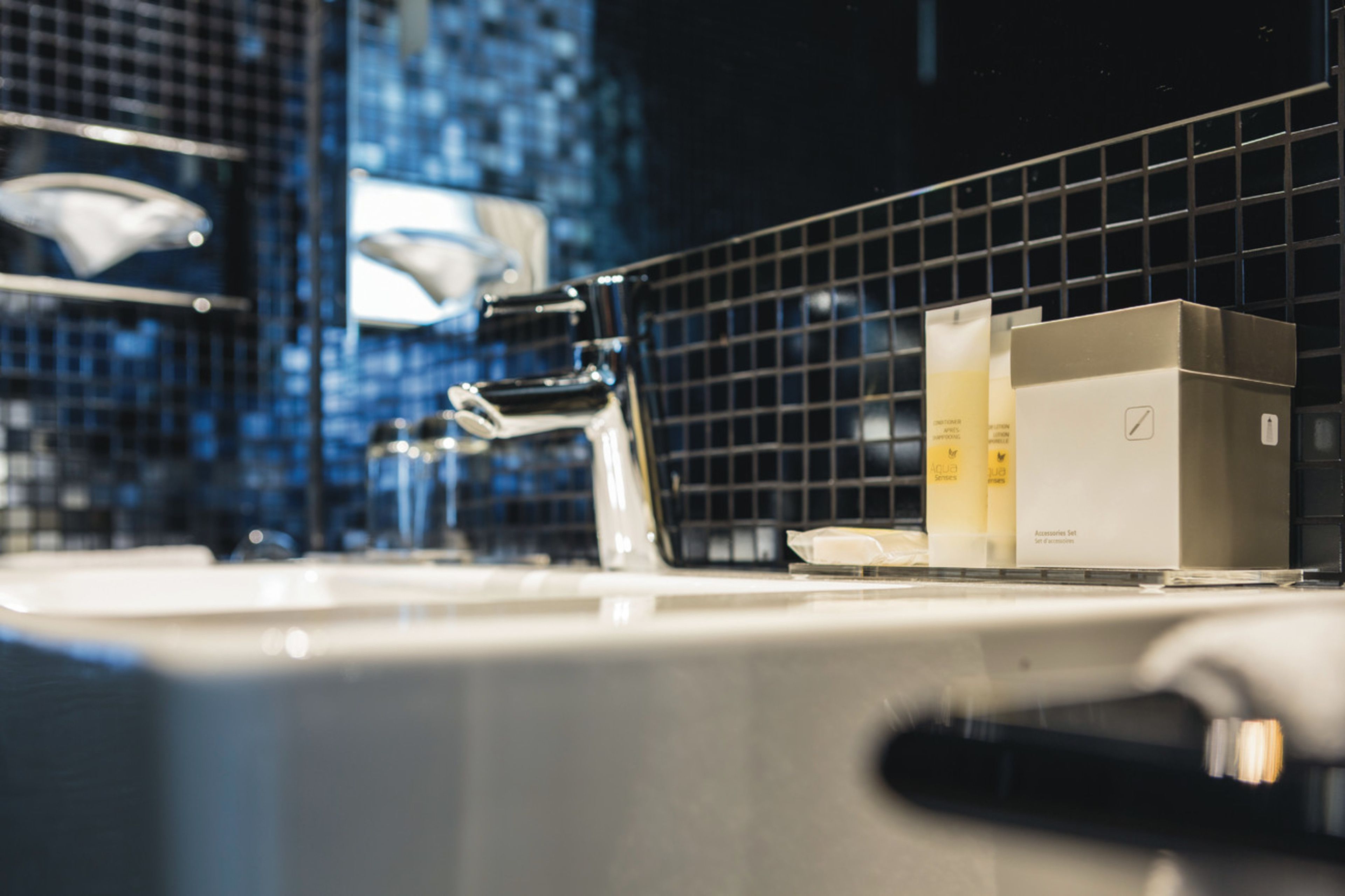 A bathroom with a modern sink, chrome faucet, and a mirror. There are toiletries on the counter.