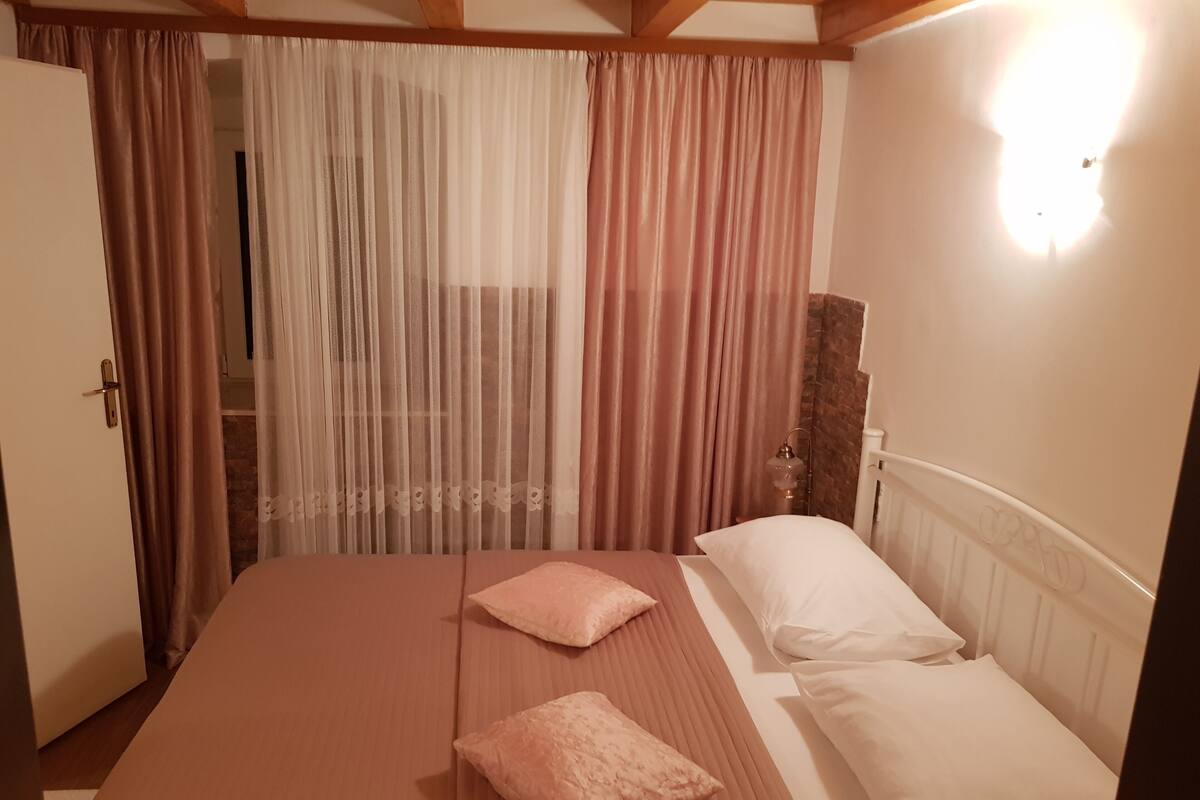 A bedroom with a bed, two pillows, a bedside lamp, and a window with curtains.