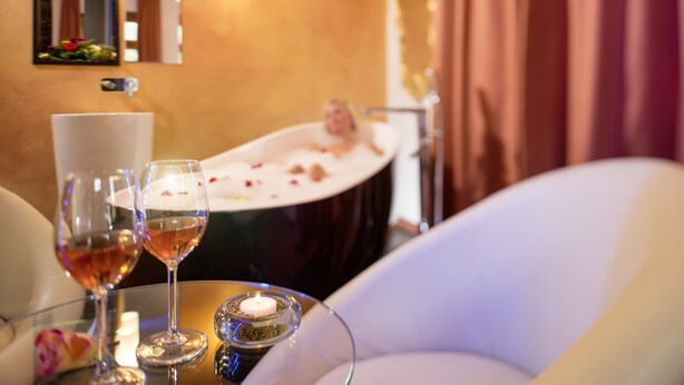 Un baño con bañera, un espejo y una mesa con dos copas de vino y una vela.