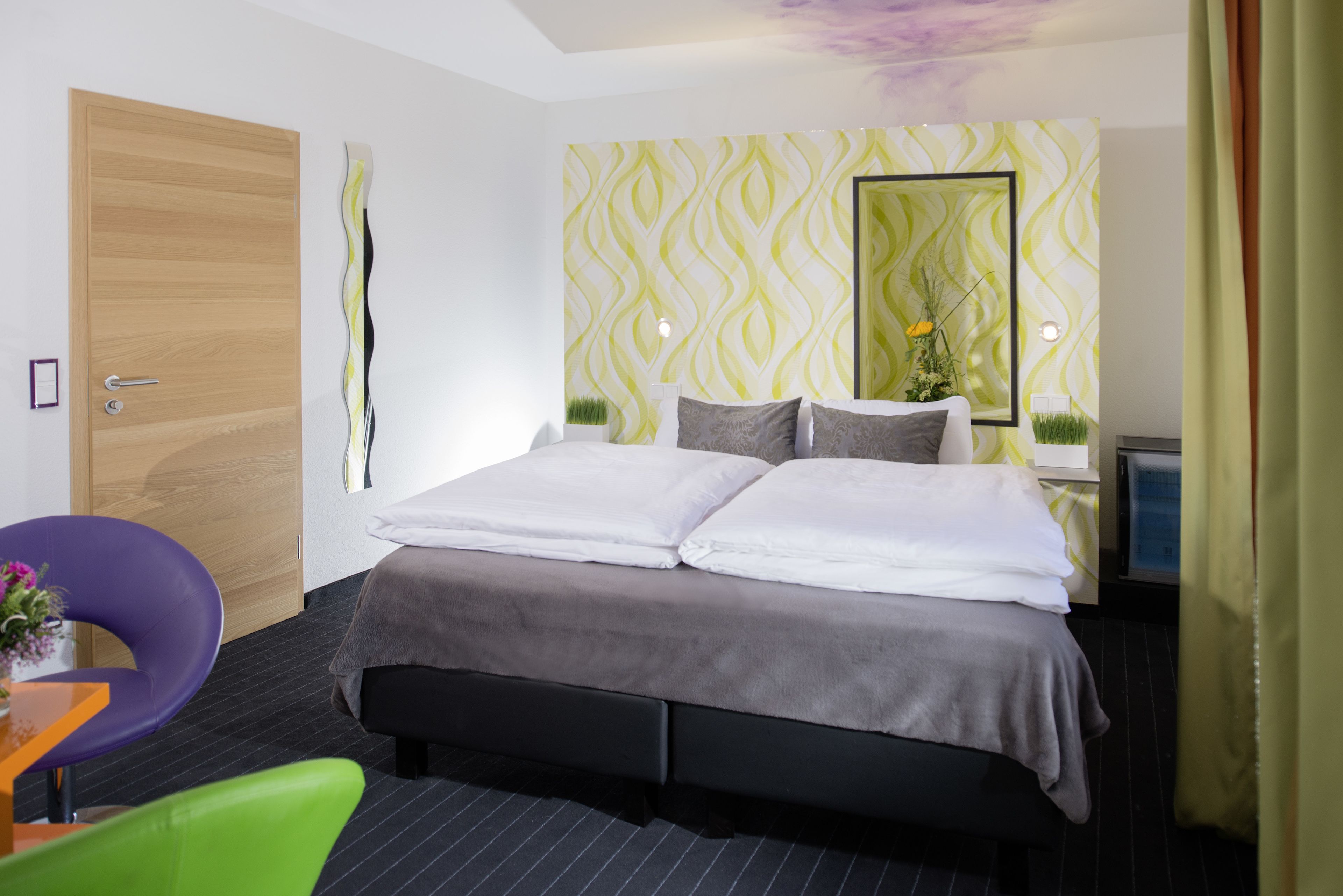 Una habitació d'hotel moderna amb un llit gran, una porta de fusta i un mirall a la paret.