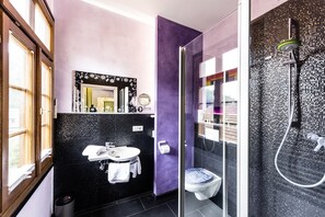 Un baño moderno con una decoración en tonos negro y morado, cabina de ducha de vidrio y un inodoro a la vista.