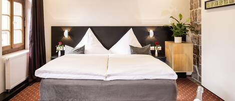 A neatly made bed with a black headboard, a potted plant, and a bottle of champagne on the nightstand.