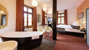 Una habitación de hotel con una bañera grande, una cama, un escritorio con una computadora y una silla.