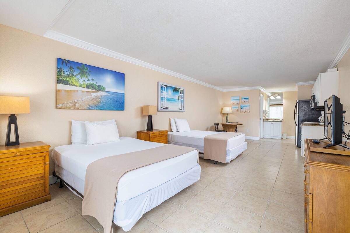 A hotel room with two beds, a desk, a refrigerator, and a TV.