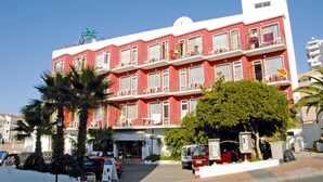 Un hotel de varios pisos con balcones, un café en la planta baja y palmeras al frente.