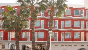 Un hotel de varios pisos con paredes exteriores rojas y blancas, balcones y palmeras al frente.