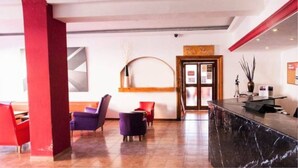 Un vestíbulo de hotel con asientos rojos y morados, un mostrador de recepción y un ventanal grande.