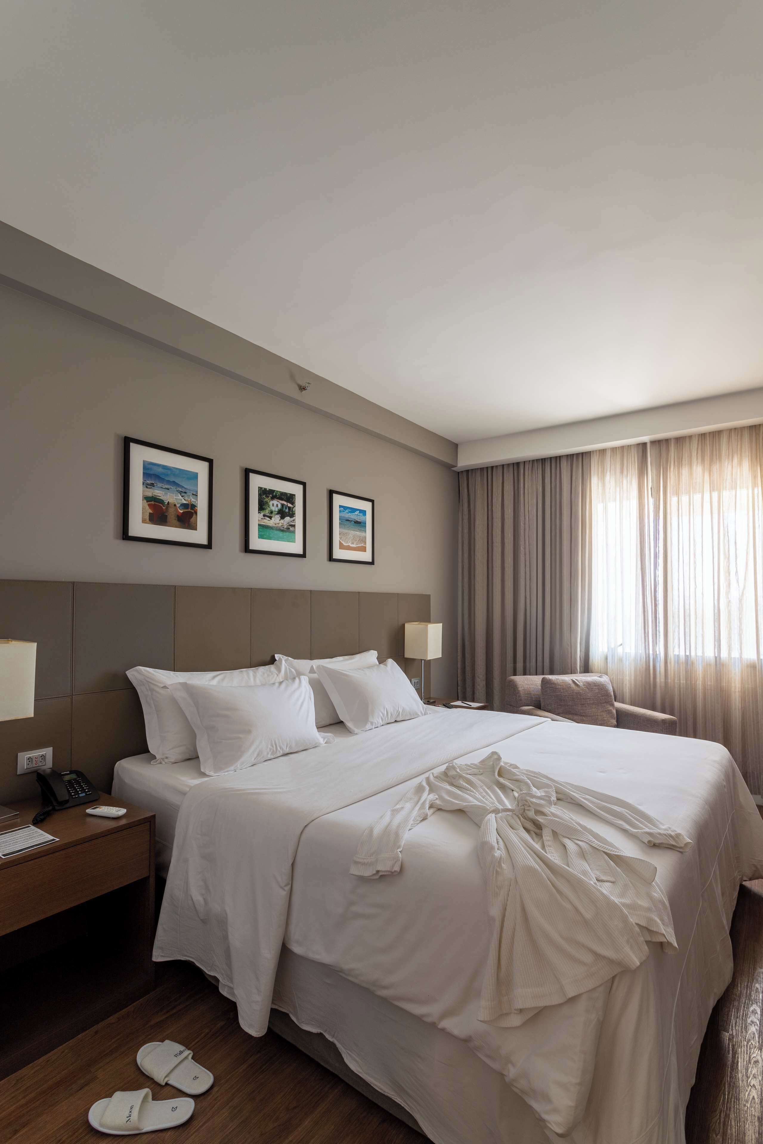 A hotel room with a large bed, a nightstand with a phone, and a chair. There are three framed pictures on the wall above the bed.