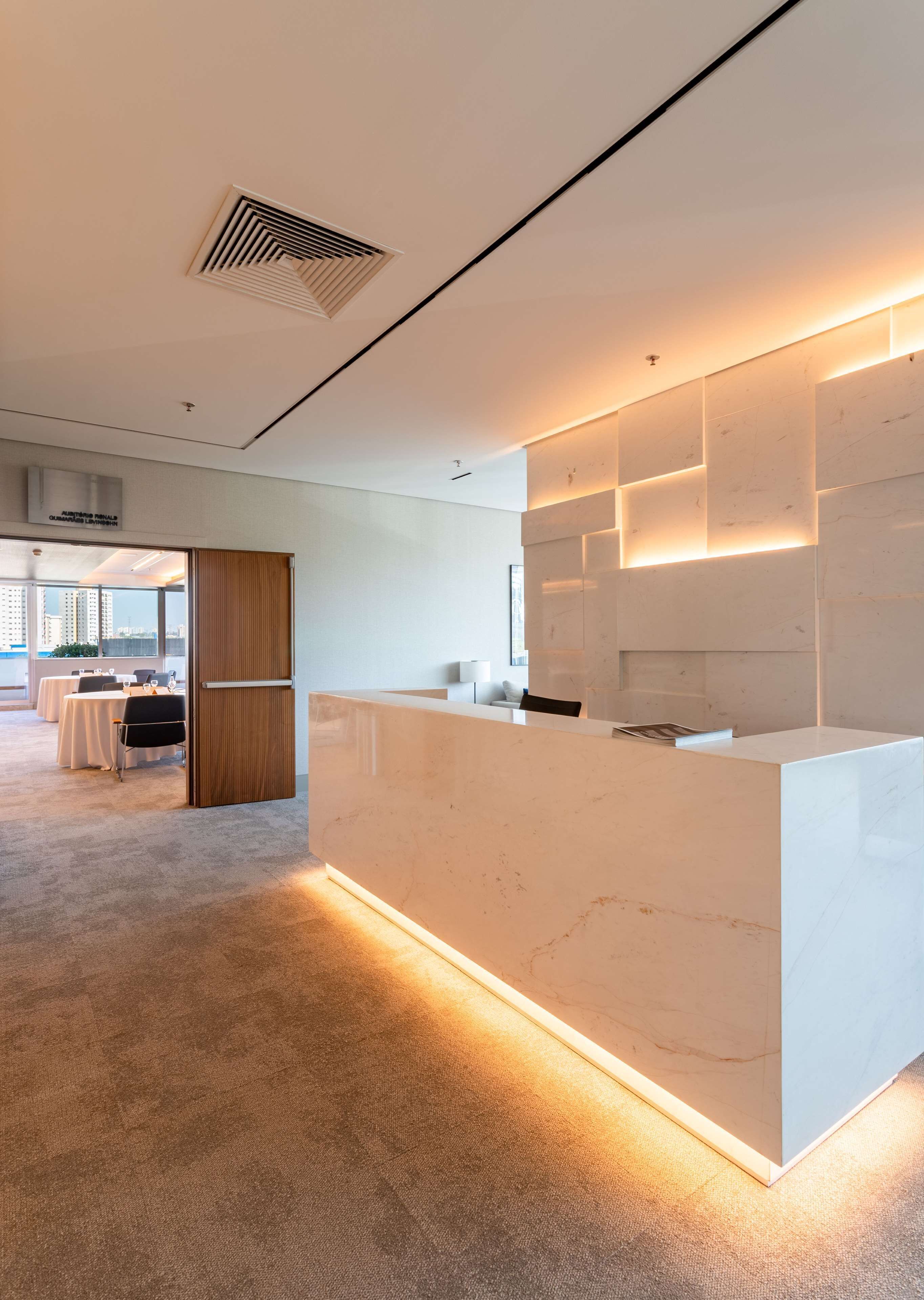 A modern reception area with a marble counter, a wooden door, and a view of a dining area with tables and chairs.