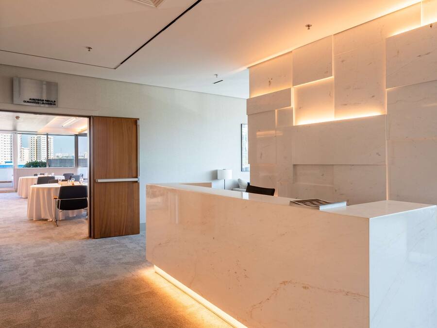 Un área de recepción moderna con un mostrador de mármol, una puerta de madera y vistas a un comedor con mesas y sillas.