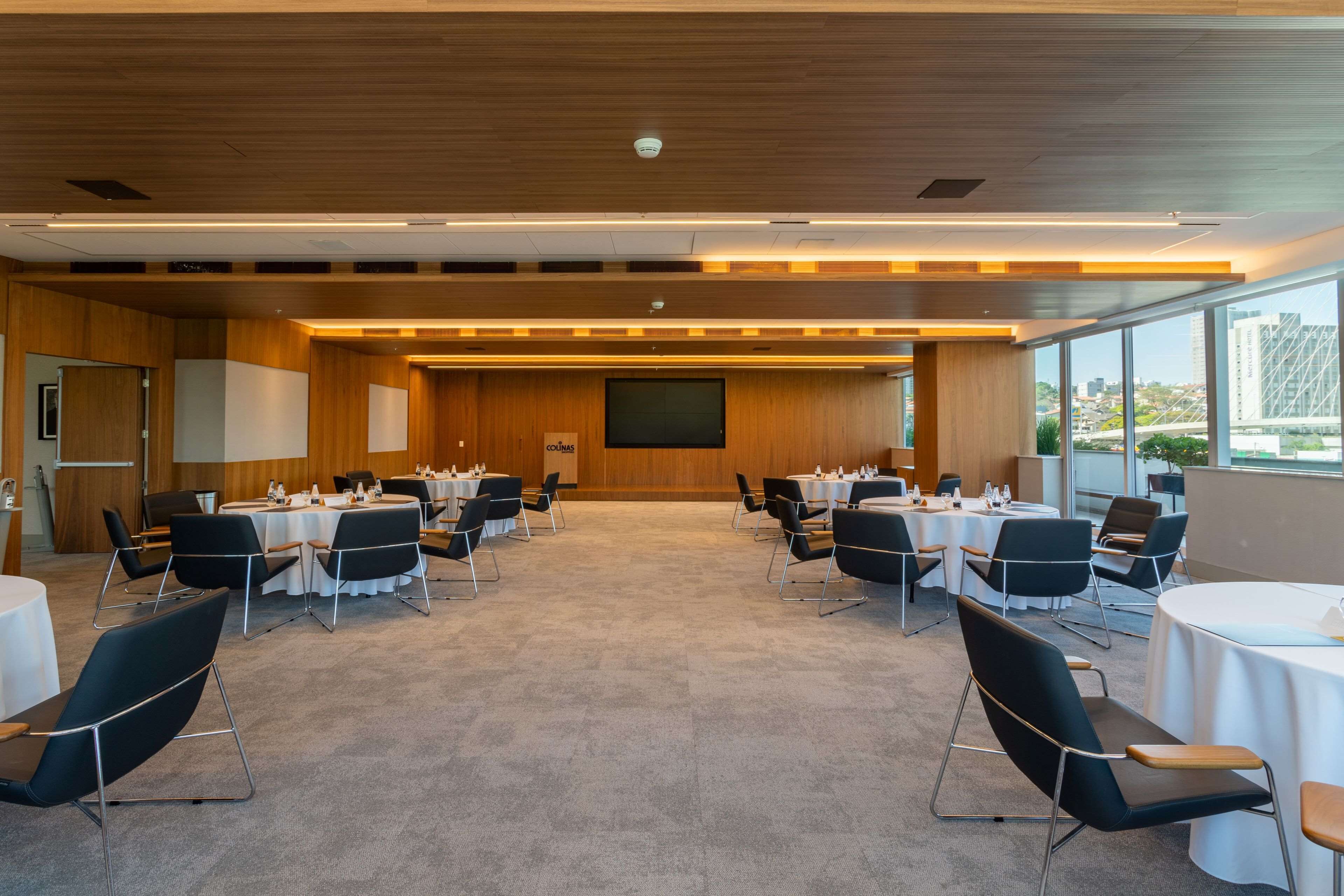 A conference room with round tables, black chairs, and a large screen at the front.