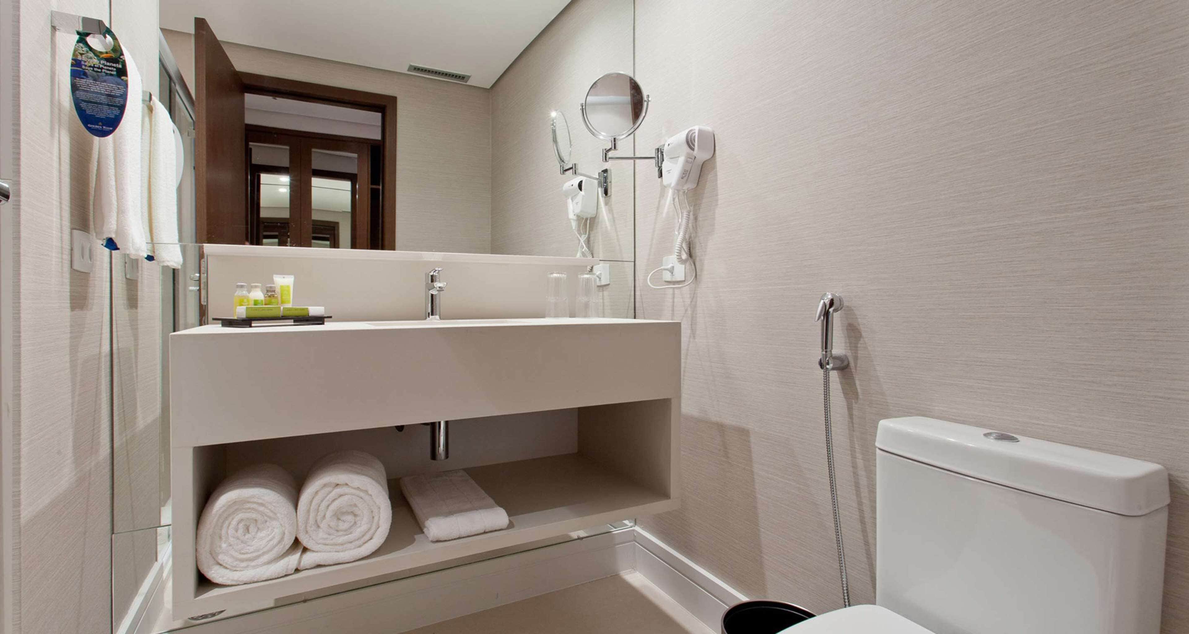 A bathroom with a toilet, a sink with a mirror, and a hairdryer on the wall.
