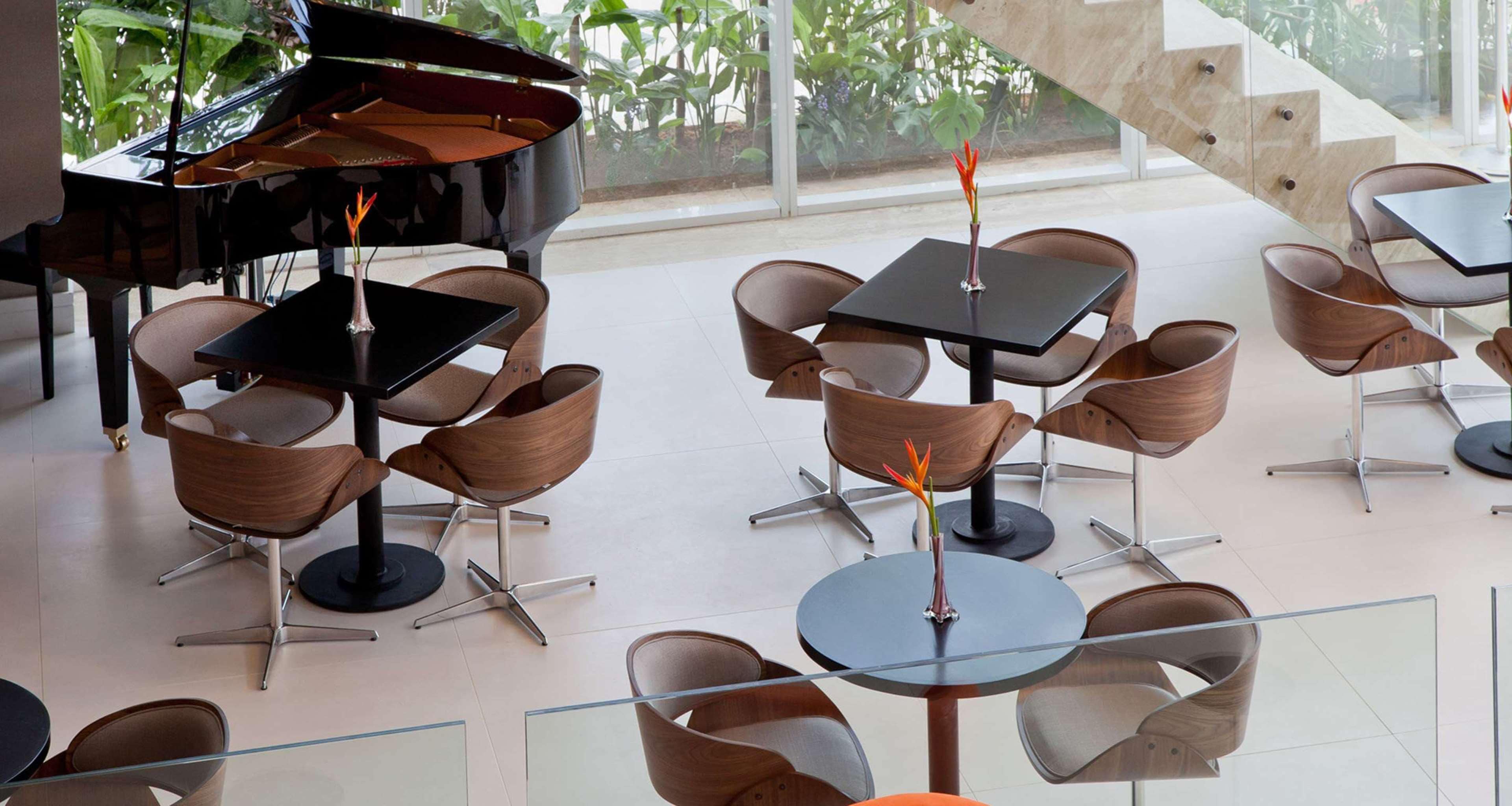 A modern indoor space with a grand piano, round tables, and contemporary chairs.